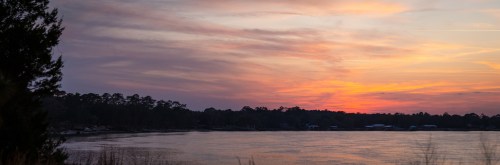 A serene sunset over a calm lake, with colorful clouds reflecting on the water and silhouettes of trees in the foreground.