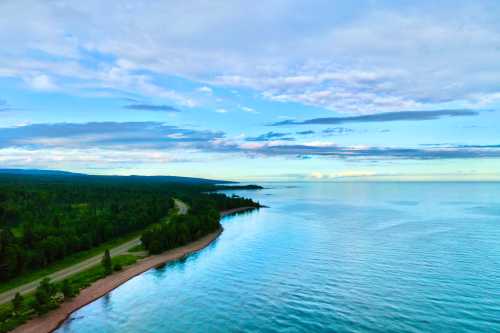 A serene lakeside view with lush greenery, a sandy shore, and a calm blue sky reflecting on the water.