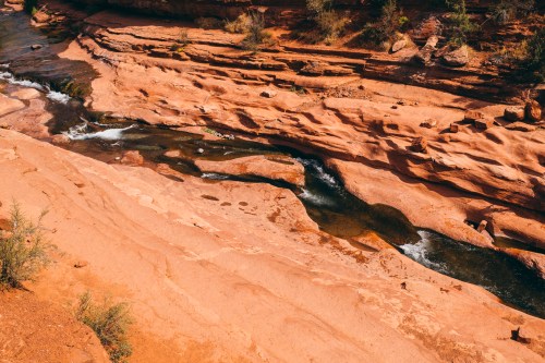 A winding river flows through rocky, reddish terrain, surrounded by sparse vegetation and steep cliffs.