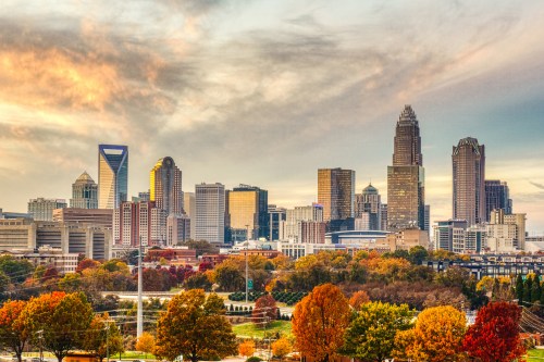 Charlotte skyline at sunset, featuring tall buildings and vibrant autumn foliage in the foreground.