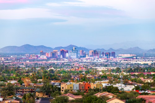 A panoramic view of a city skyline with mountains in the background, featuring modern buildings and greenery in the foreground.