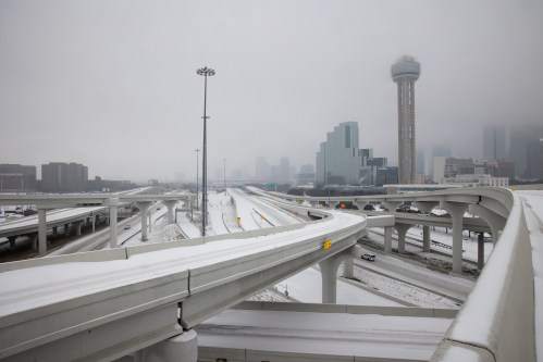 A snowy urban landscape featuring highways and a tall tower in the background, shrouded in fog.