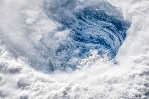 A swirling pattern of clouds surrounding a clear blue area, resembling a storm system from above.