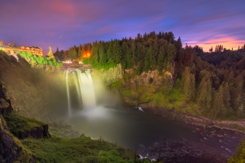 A serene waterfall cascades into a calm river, surrounded by lush trees under a colorful twilight sky.