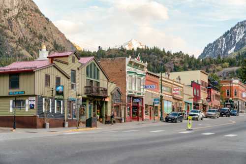 A charming mountain town street lined with colorful historic buildings and shops, surrounded by scenic mountains.