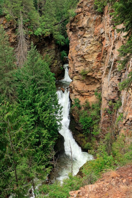 A waterfall cascades through a rocky canyon, surrounded by lush green trees and steep cliffs.