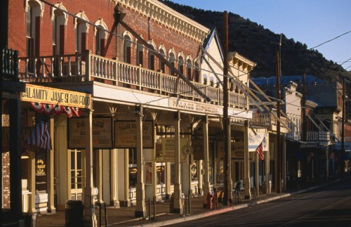 Historic buildings line a street in a western town, with flags and signage under warm evening light.
