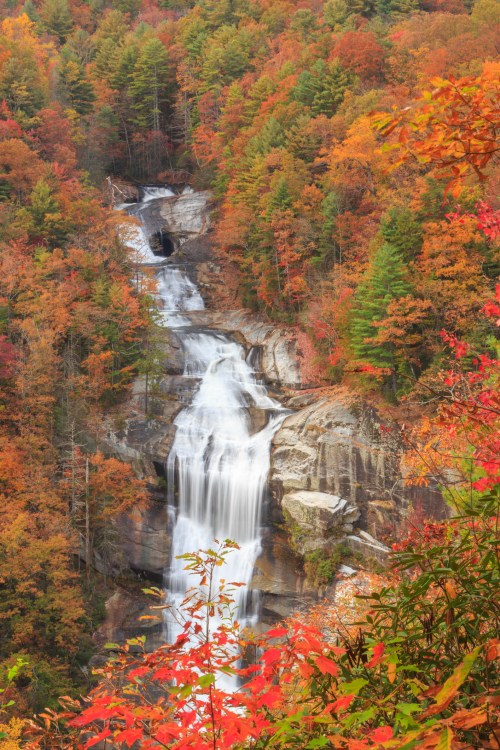 A cascading waterfall surrounded by vibrant autumn foliage in shades of red, orange, and green.
