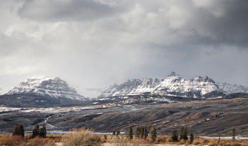 Snow-capped mountains under a cloudy sky, with a foreground of rolling hills and sparse vegetation.