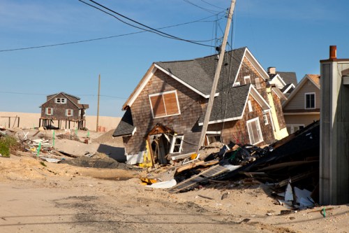 A damaged neighborhood with leaning houses and debris, showing the aftermath of a natural disaster.
