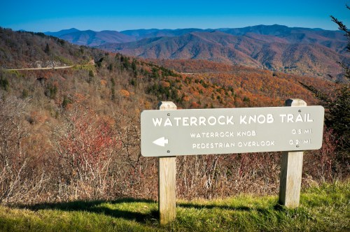 A sign for Waterrock Knob Trail with scenic mountains and autumn foliage in the background.