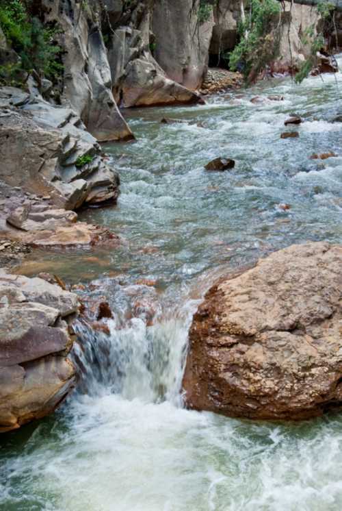 A flowing river cascades over rocks, surrounded by lush greenery and rugged cliffs.