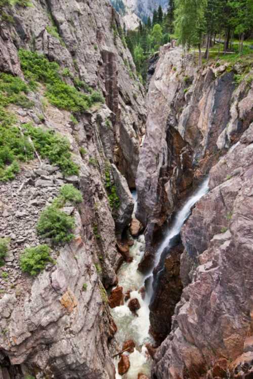 A narrow canyon with steep rocky walls and a rushing river flowing through the bottom, surrounded by greenery.