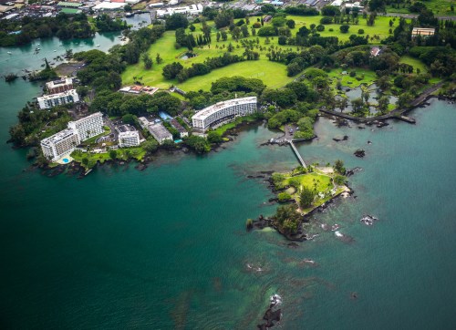 Aerial view of lush green landscape with buildings along the water's edge and rocky shoreline.