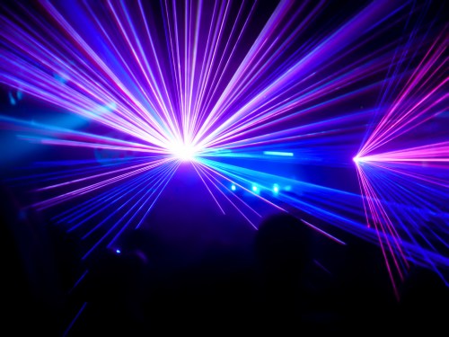 Colorful laser lights create a vibrant display in a dark setting, illuminating the atmosphere with purple and blue beams.