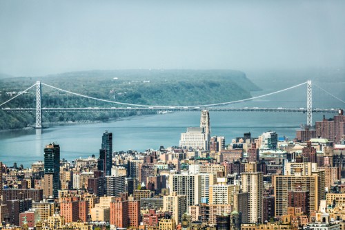 A panoramic view of a city skyline with a bridge spanning a river and green hills in the background.