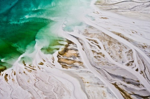 Aerial view of a vibrant turquoise body of water meeting sandy, textured shorelines with intricate patterns.