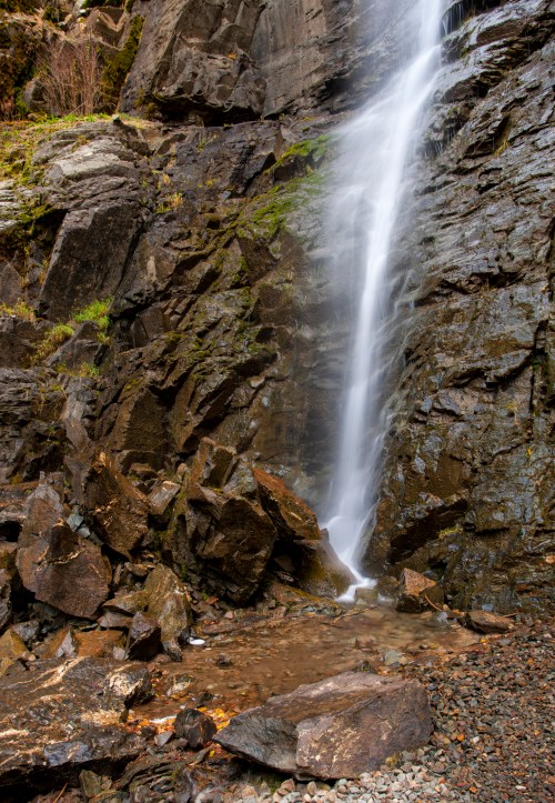 A serene waterfall cascading down rocky cliffs, surrounded by moss and stones, creating a tranquil natural scene.