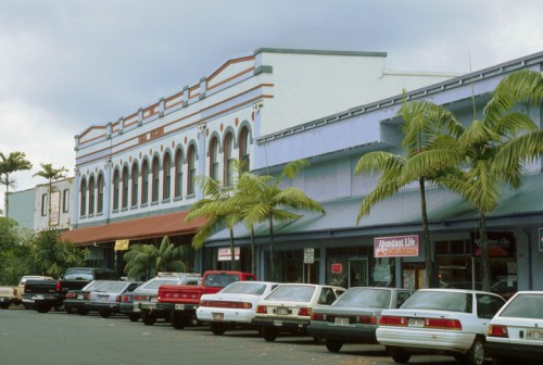 Historic buildings with colorful facades line a street, featuring palm trees and parked cars in front.