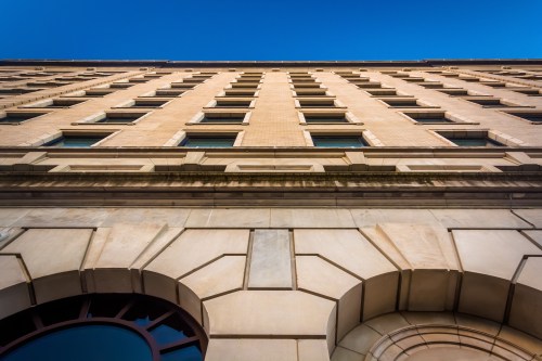 View of a tall building from below, showcasing its architectural details and windows against a clear blue sky.