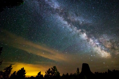 A stunning night sky filled with stars and the Milky Way, with a silhouette of trees and a distant rock formation.