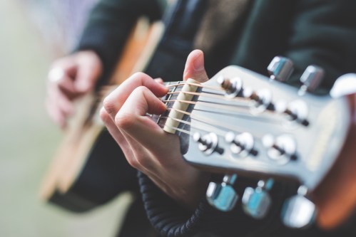 A close-up of a person's hand playing an acoustic guitar, focusing on the strings and tuning pegs.