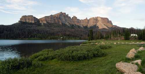 Scenic view of a lake surrounded by lush greenery and towering mountains under a clear sky.