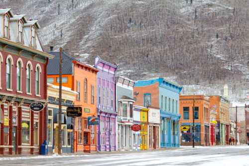 Colorful historic buildings line a snowy street, set against a backdrop of a mountain.