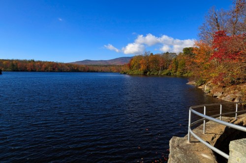 A serene lake surrounded by autumn foliage under a clear blue sky, with mountains in the background.