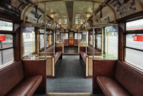Interior of a vintage tram, featuring wooden benches and a spacious aisle, with newspaper decor on the walls.