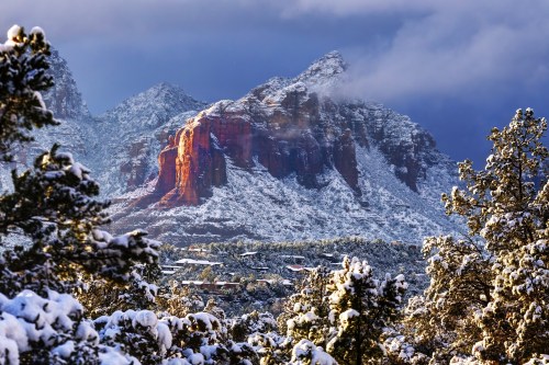 Snow-covered mountains under a dramatic sky, with sunlight illuminating a rocky peak in the distance.