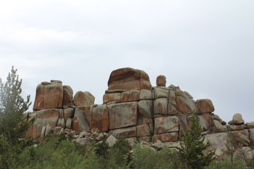 A rugged rock formation with large boulders, surrounded by greenery under a cloudy sky.