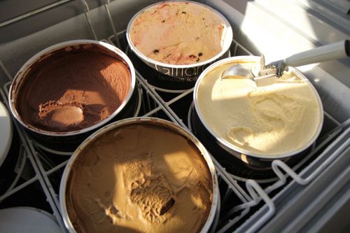 Four tubs of ice cream in a freezer, featuring chocolate, coffee, and vanilla flavors.