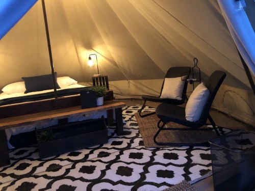 Cozy glamping tent interior with a bed, seating area, and decorative rug. Warm lighting creates a welcoming atmosphere.