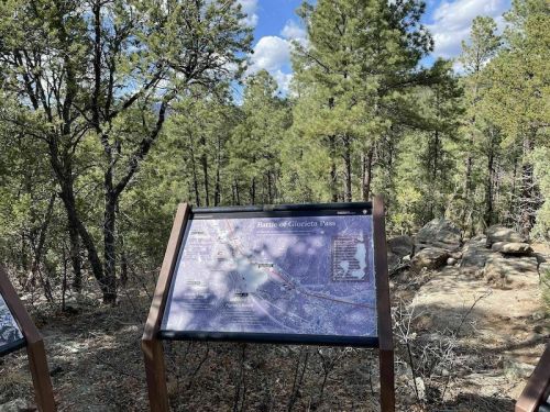 A map display in a forested area, surrounded by pine trees, showing the route of the Battle of Glorieta Pass.