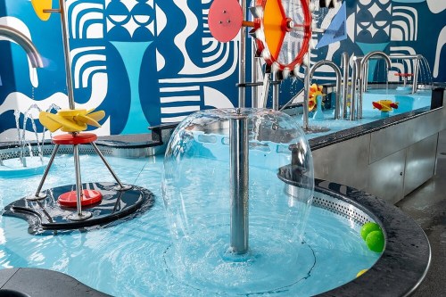 A colorful water play area featuring interactive water features, including a spinning wheel and water jets.