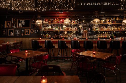 Cozy bar interior with dim lighting, wooden tables, and a well-stocked bar adorned with string lights and candles.