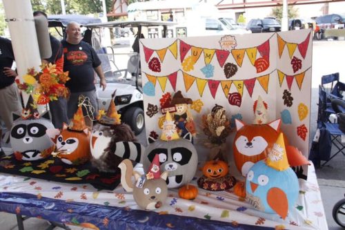 A festive display of decorated pumpkins and autumn-themed decorations at a fall event, with colorful banners in the background.