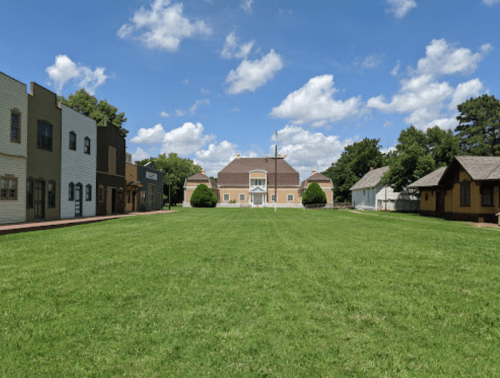 A wide grassy area with a historic building in the center, surrounded by various styled buildings under a blue sky.