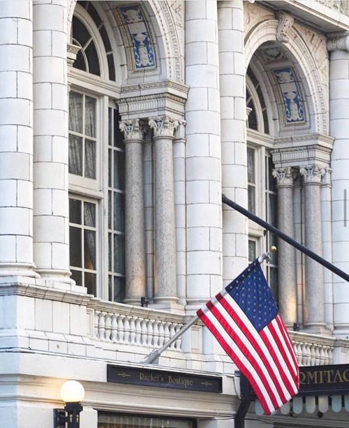 A historic building with ornate columns and large windows, featuring an American flag in front.
