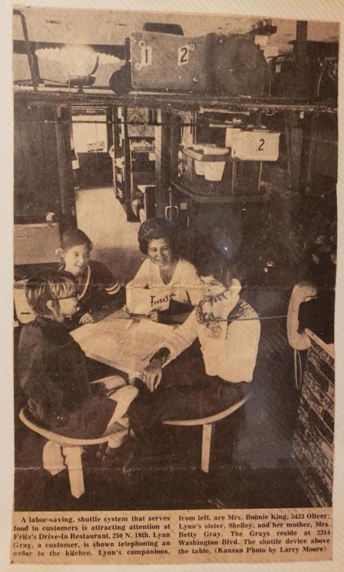 A woman and two girls sit at a table in a restaurant, showcasing a food shuttle system in the background.