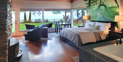 Cozy bedroom with a large window view, featuring a bed, seating area, and a beautiful outdoor landscape.