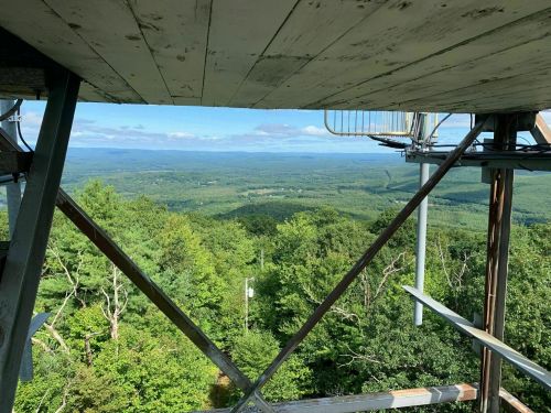 View from a tower overlooking a lush green landscape and distant mountains under a clear blue sky.