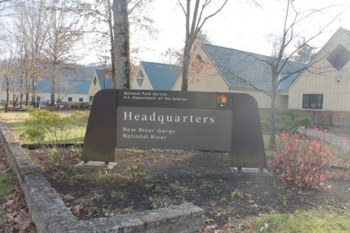 Sign for the National Park Service Headquarters at New River Gorge National River, surrounded by trees and buildings.
