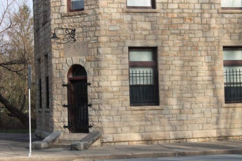 Historic stone bank building with barred windows and a decorative entrance, set in a quiet area.