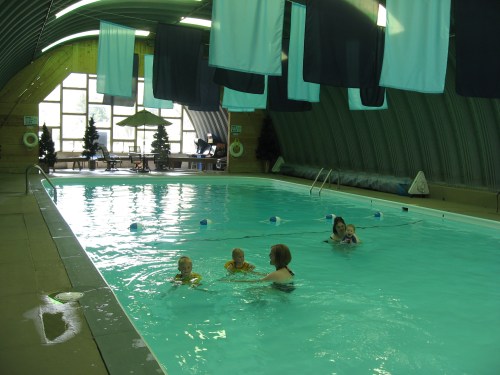 Indoor swimming pool with children and an adult enjoying the water, surrounded by colorful hanging fabric.