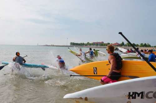 A group of people surfing and paddling on a calm lake, with some splashing water and colorful boards.