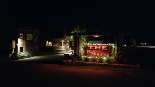 A dimly lit sign reading "The Barn" adorned with lights, set against a dark night backdrop.