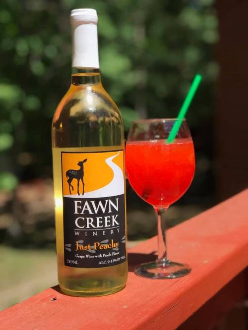 A bottle of Fawn Creek Winery First Peachy wine next to a red cocktail in a glass with a green straw.