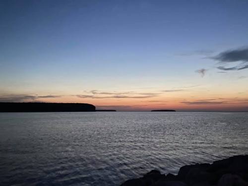 A serene sunset over calm waters, with silhouettes of distant islands and a gradient sky transitioning from blue to orange.